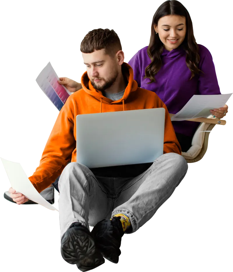 Two students studying together, one working on a laptop while the other reviews her notes